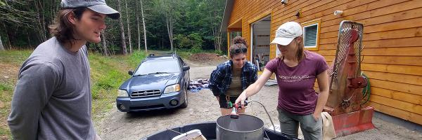 Rob Fitch, Rhona Thomson, and Jess Colby operate the Dybvig, a tool to clean seed. Photo courtesy of Jess Colby, NorthWoods Stewardship Center Three workers use a tool to clean seed.
